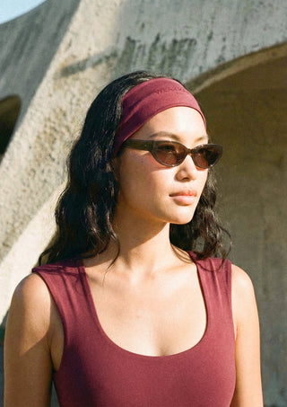 Woman wearing a maroon headband and tank top in front of a textured wall.